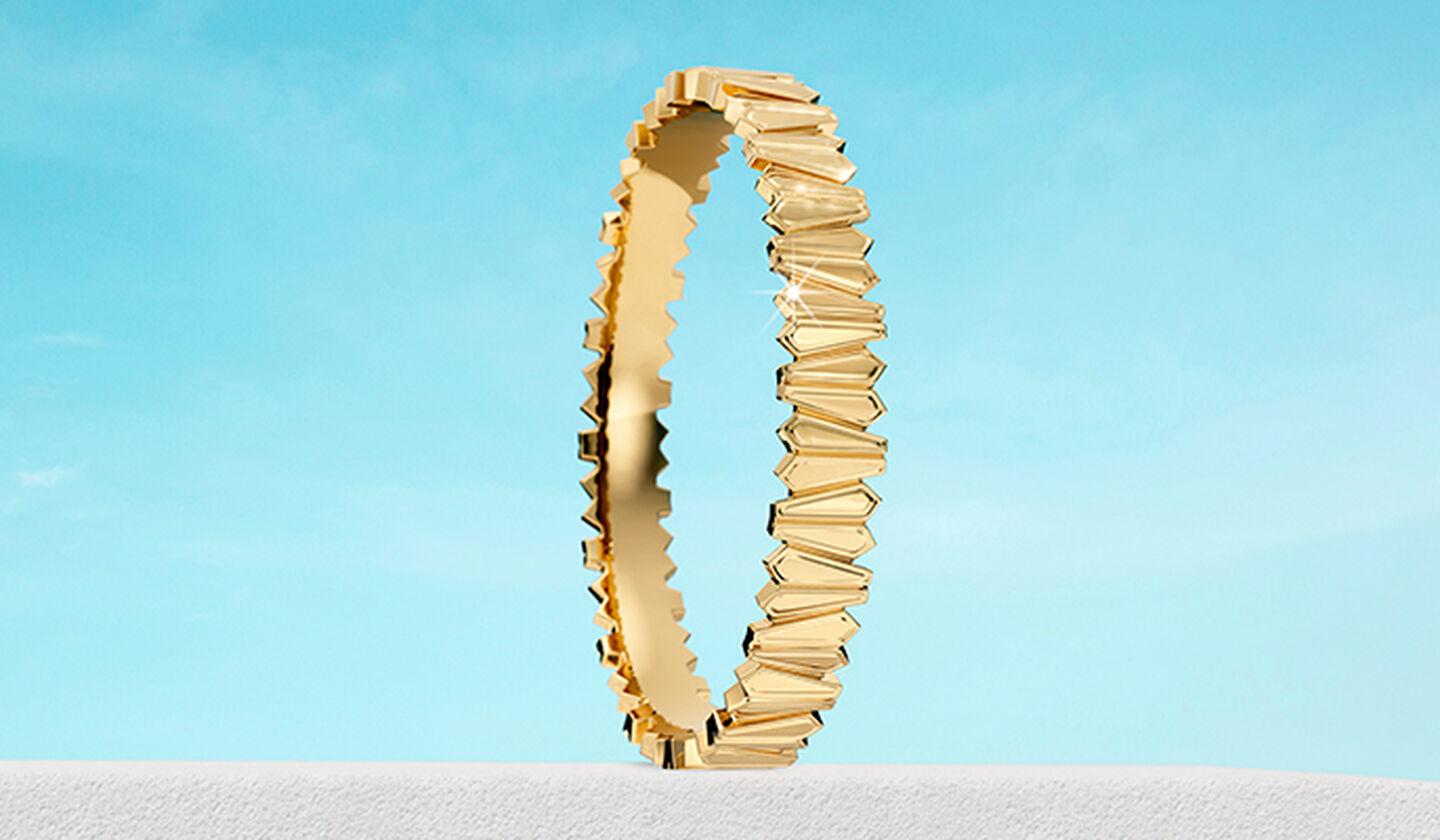 Birks Beekeeper yellow gold bangle on a blue background.